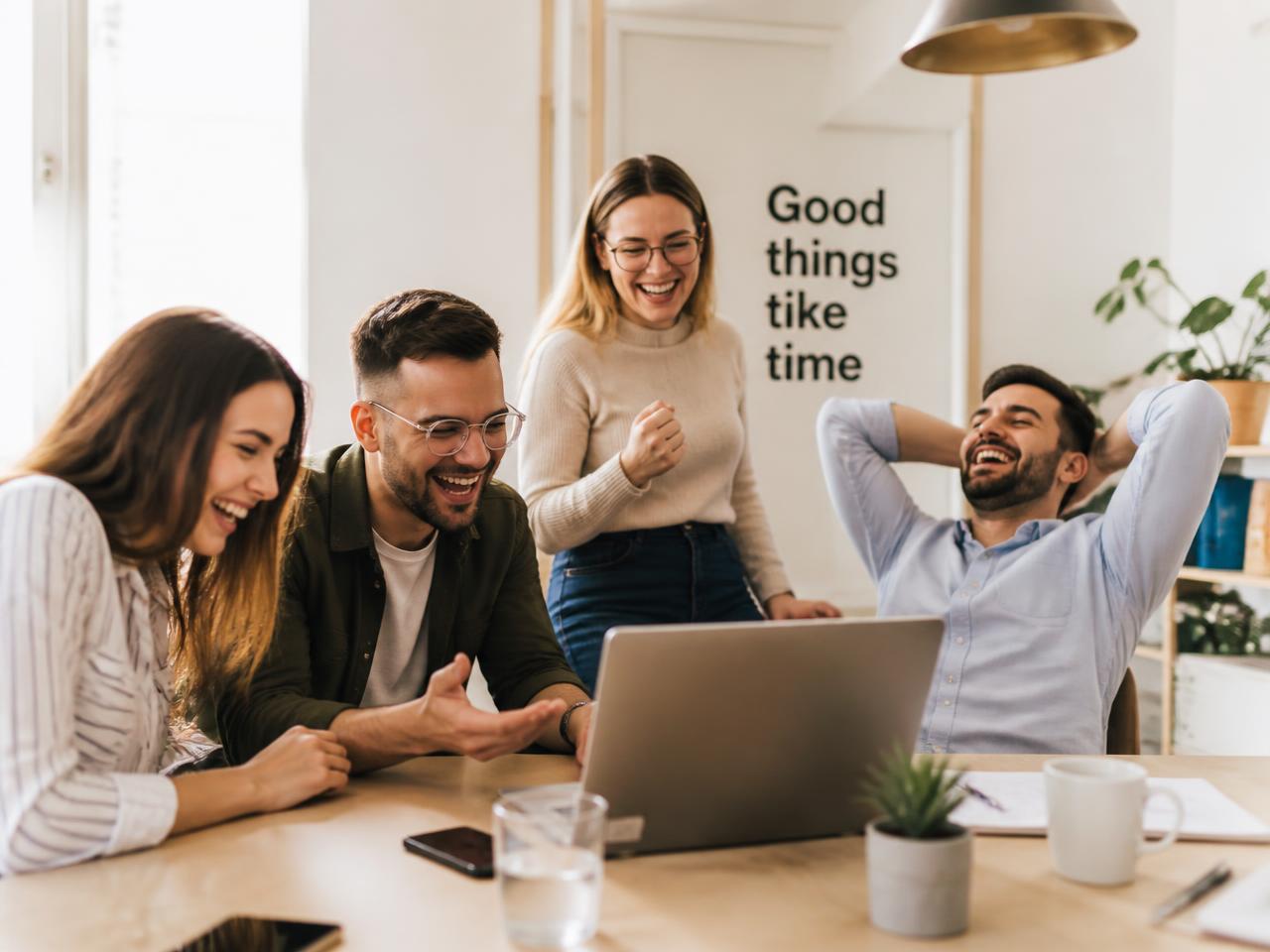 Business team laughing and looking relieved around a laptop
